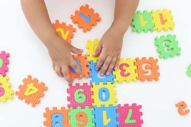 Photo of Little girl playing with colorful puzzles at white table, top view. Educational toy