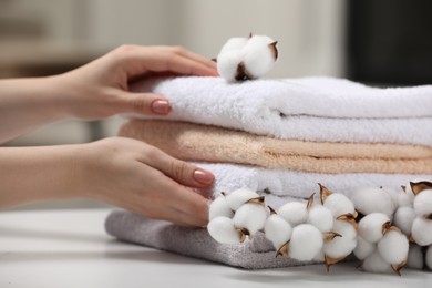 Photo of Woman taking terry towels and cotton flowers on white table indoors, closeup