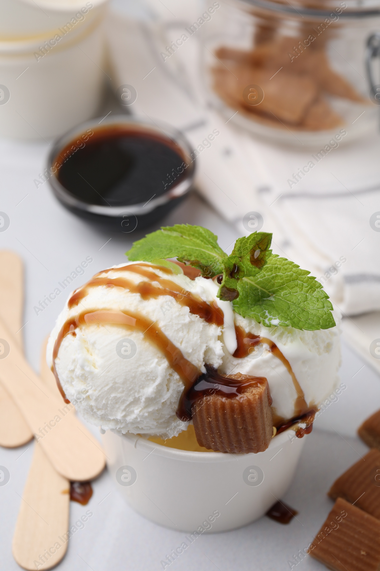 Photo of Scoops of tasty ice cream with caramel sauce, mint leaves and candies on white table, closeup