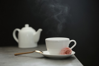 Photo of Cup of tea, saucer and spoon on table against dark background