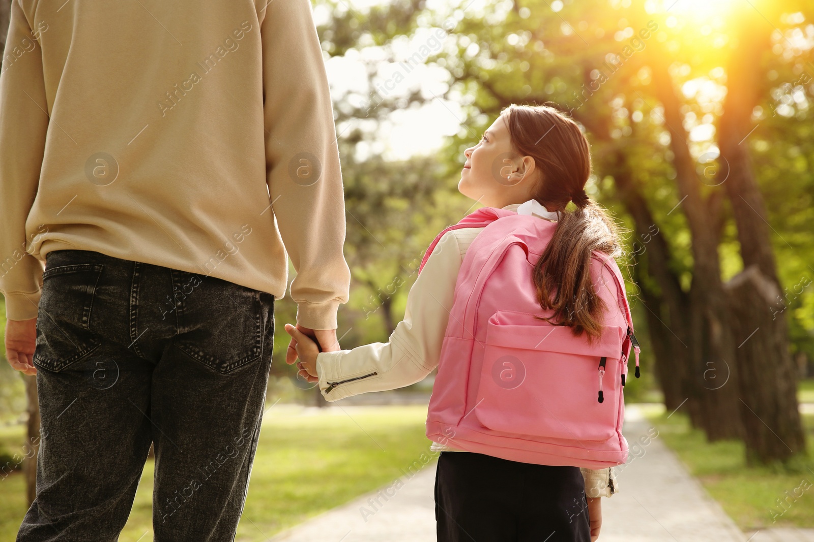 Image of Father taking his little daughter to school through park, back view