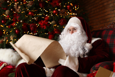 Santa Claus reading wish list in armchair near Christmas tree