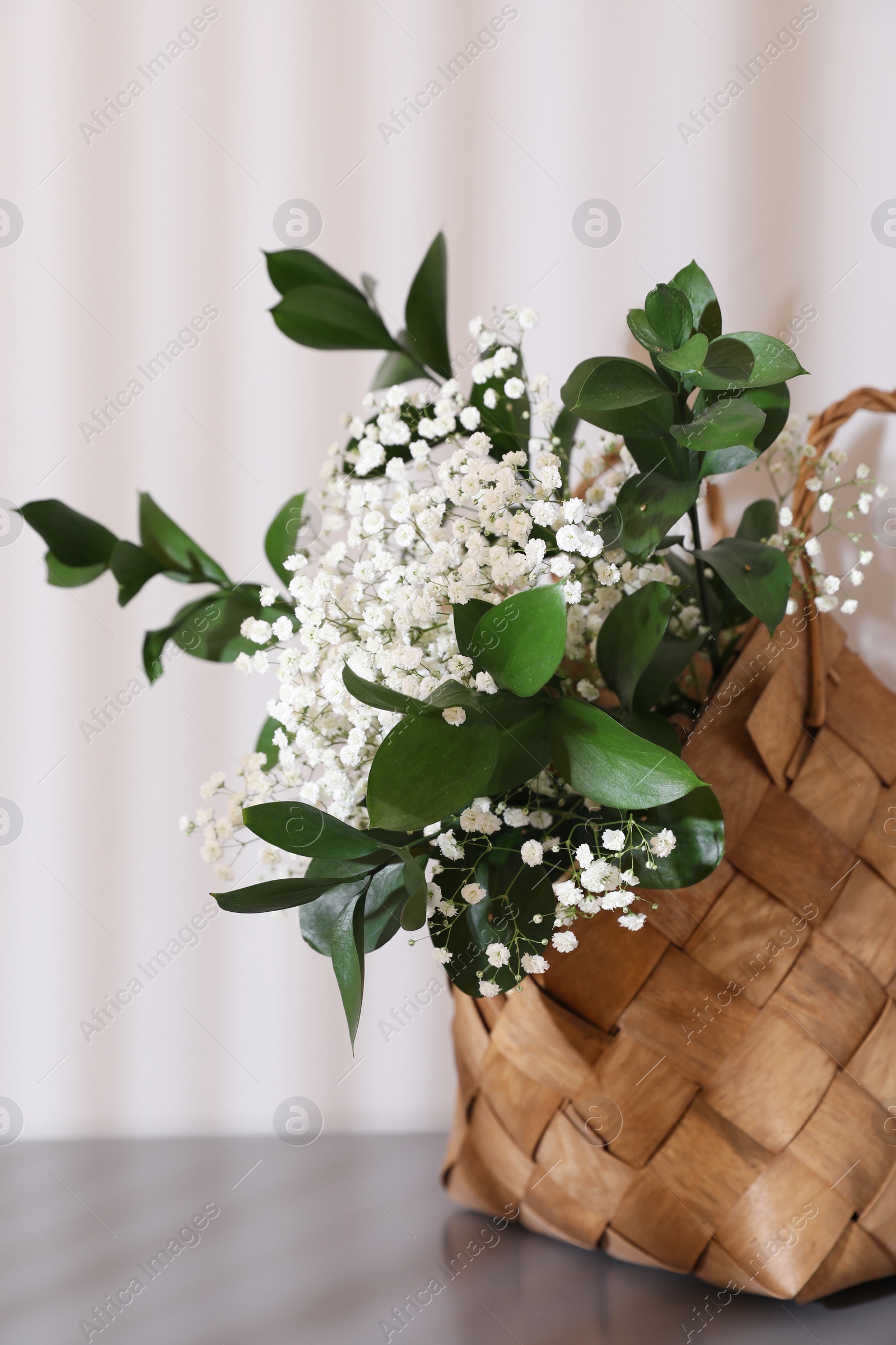 Photo of Stylish wicker basket with bouquet of flowers on wooden table indoors