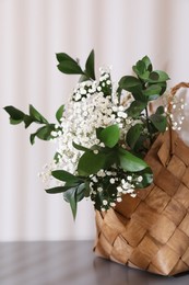 Stylish wicker basket with bouquet of flowers on wooden table indoors