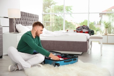 Young man packing suitcase for summer journey at home