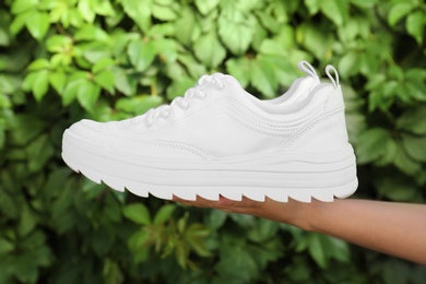 Photo of Woman holding stylish sneakers on blurred background