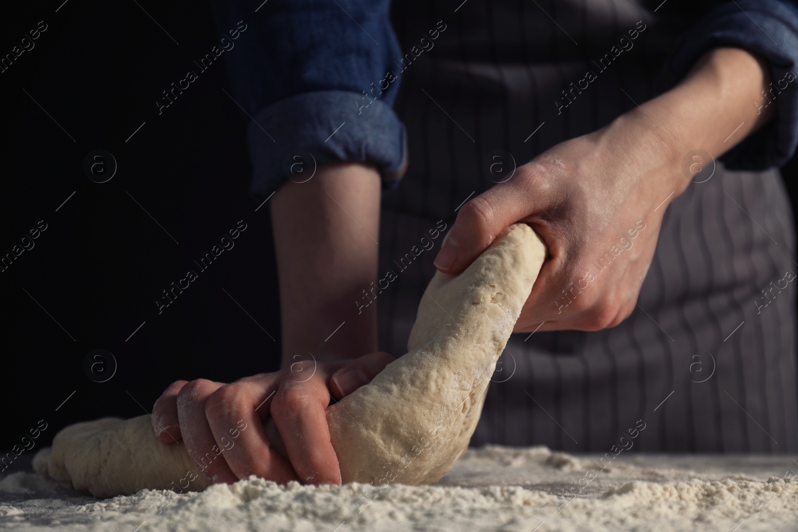 Photo of Making bread. Woman kneading dough at table on dark background, closeup