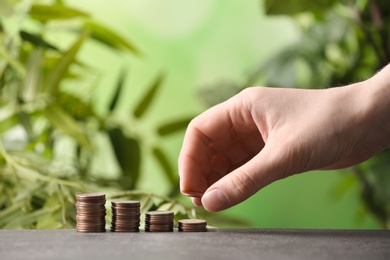 Woman stacking coins on table against blurred background, closeup. Space for text