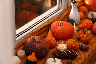 Photo of Composition with pumpkins and burning candles on window sill indoors