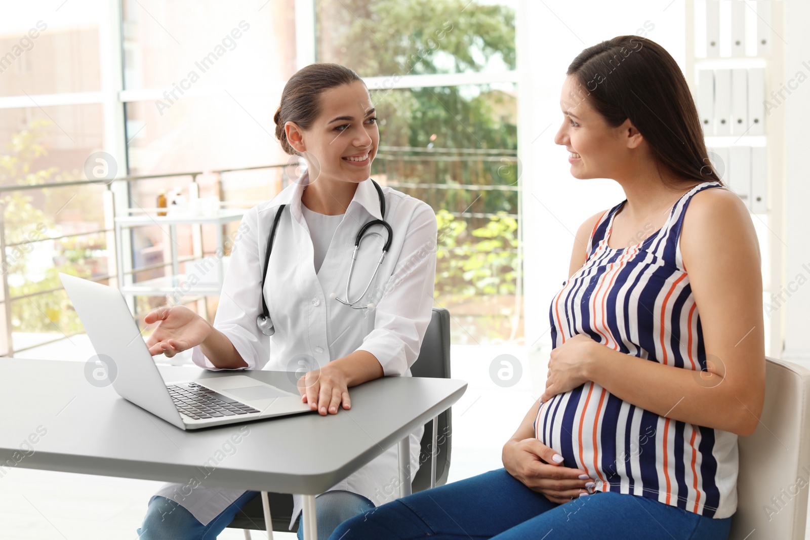 Photo of Young doctor with pregnant woman in hospital. Patient consultation