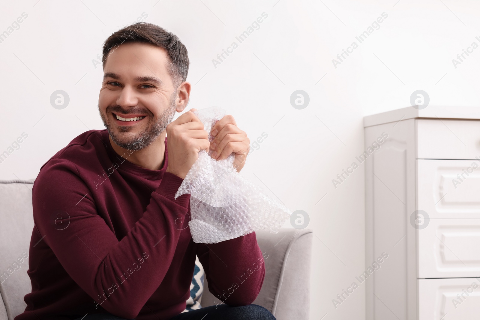 Photo of Happy man with bubble wrap indoors. Space for text