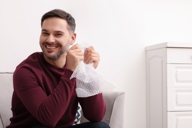 Happy man with bubble wrap indoors. Space for text