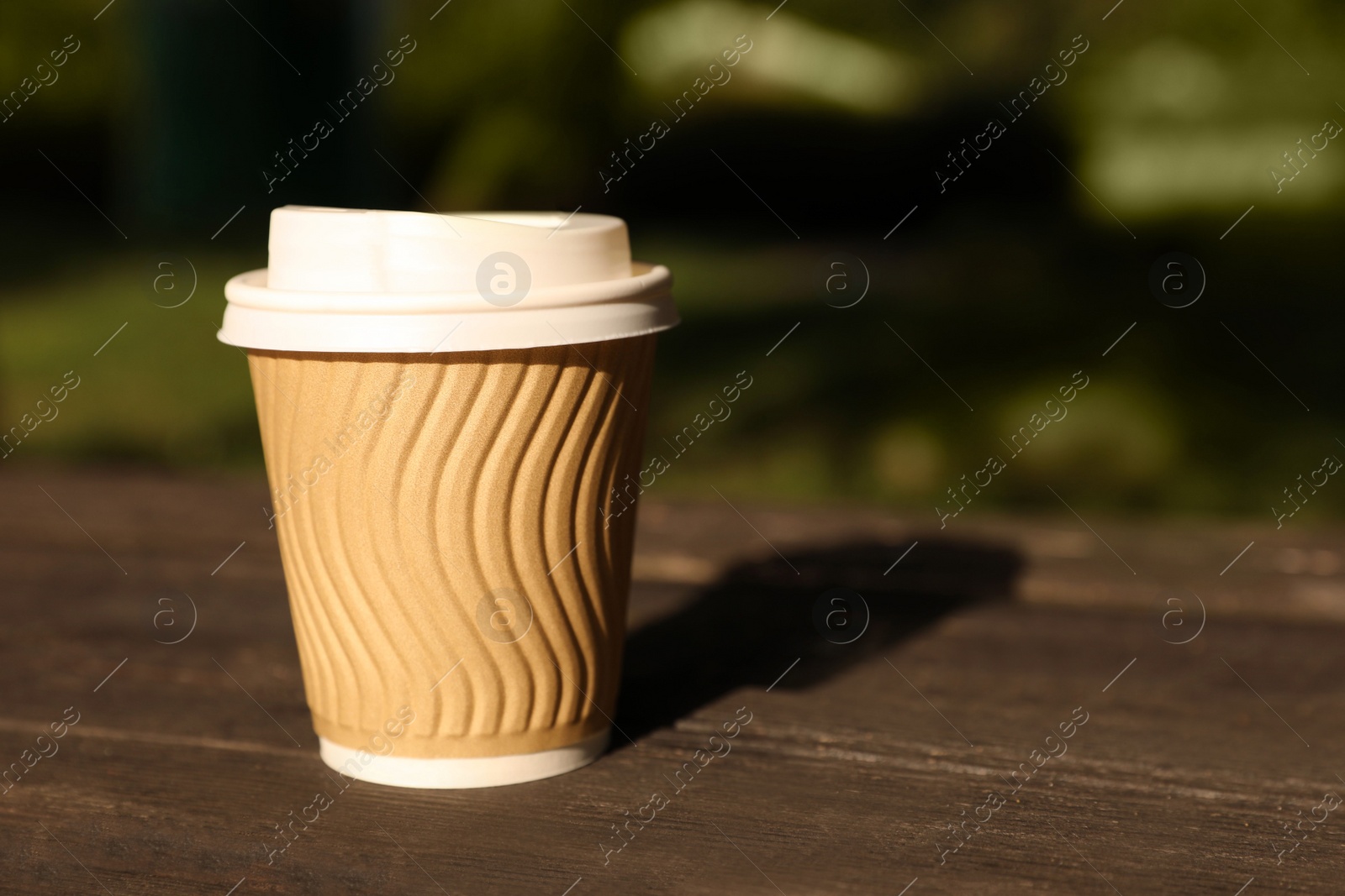 Photo of Paper cup on wooden table outdoors, closeup with space for text. Coffee to go