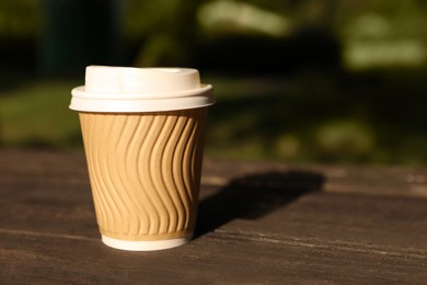 Photo of Paper cup on wooden table outdoors, closeup with space for text. Coffee to go