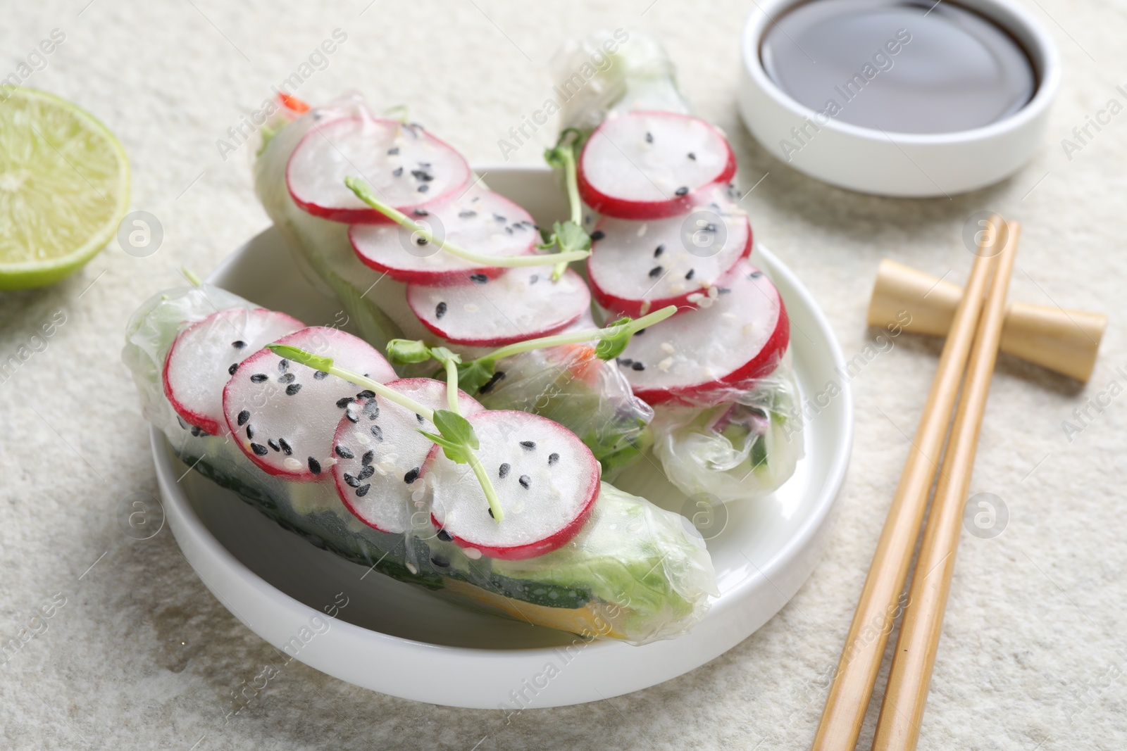 Photo of Delicious spring rolls, chopsticks, soy sauce and lime on light grey table, closeup