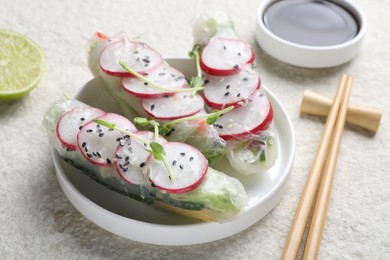 Delicious spring rolls, chopsticks, soy sauce and lime on light grey table, closeup