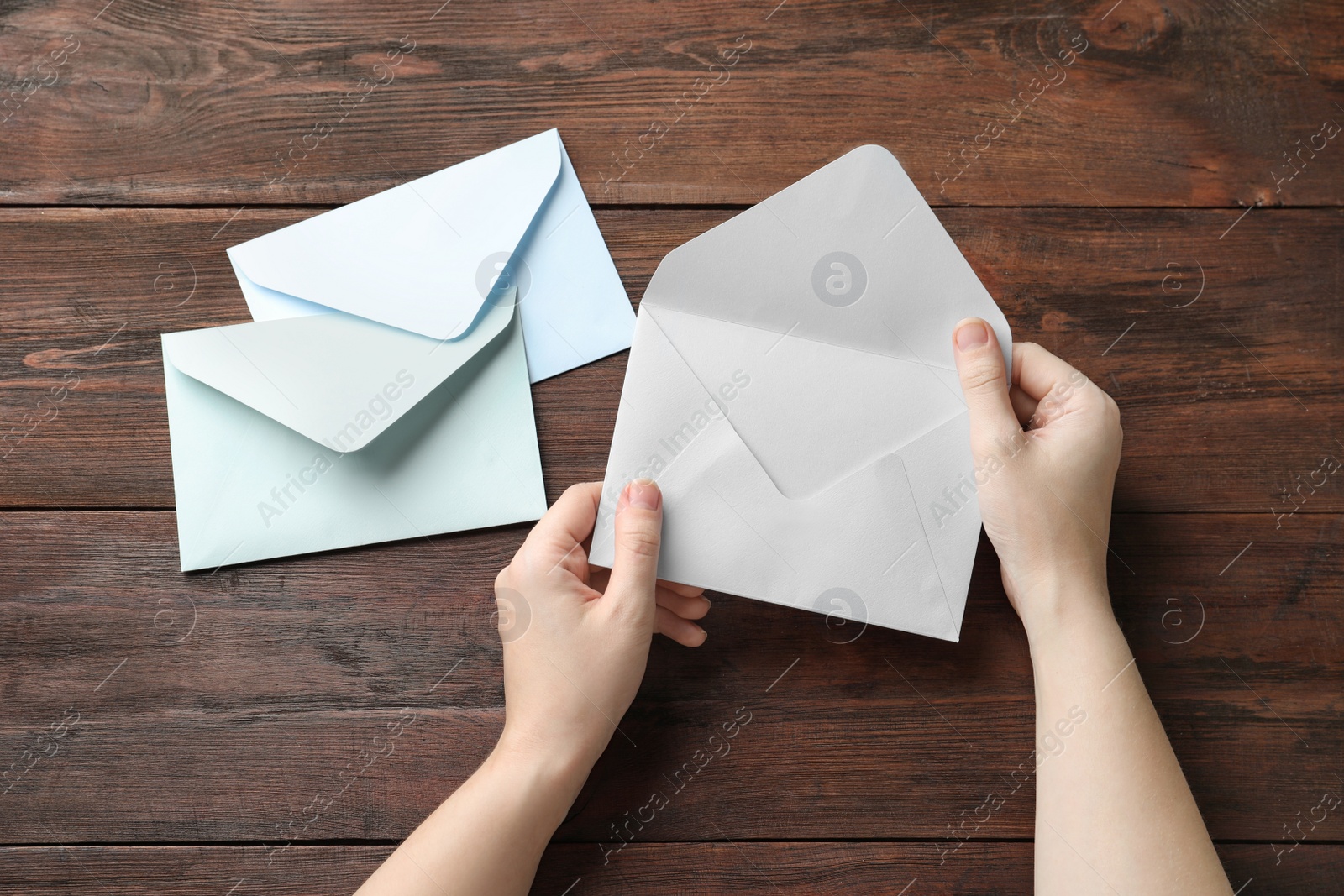 Photo of Woman with paper envelopes at wooden table, top view