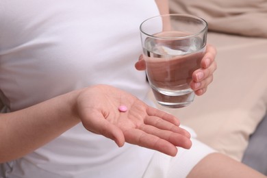 Photo of Woman with glass of water and pill indoors, closeup