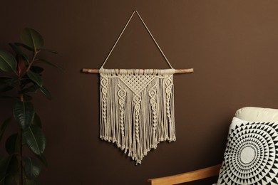 Photo of Beautiful macrame hanging on brown wall in room. Decorative element