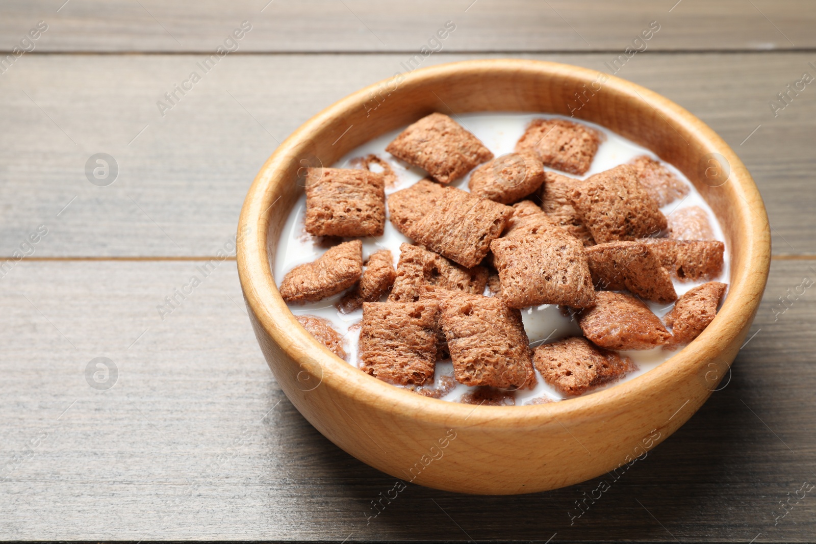 Photo of Tasty corn pads with milk in bowl on wooden table, closeup