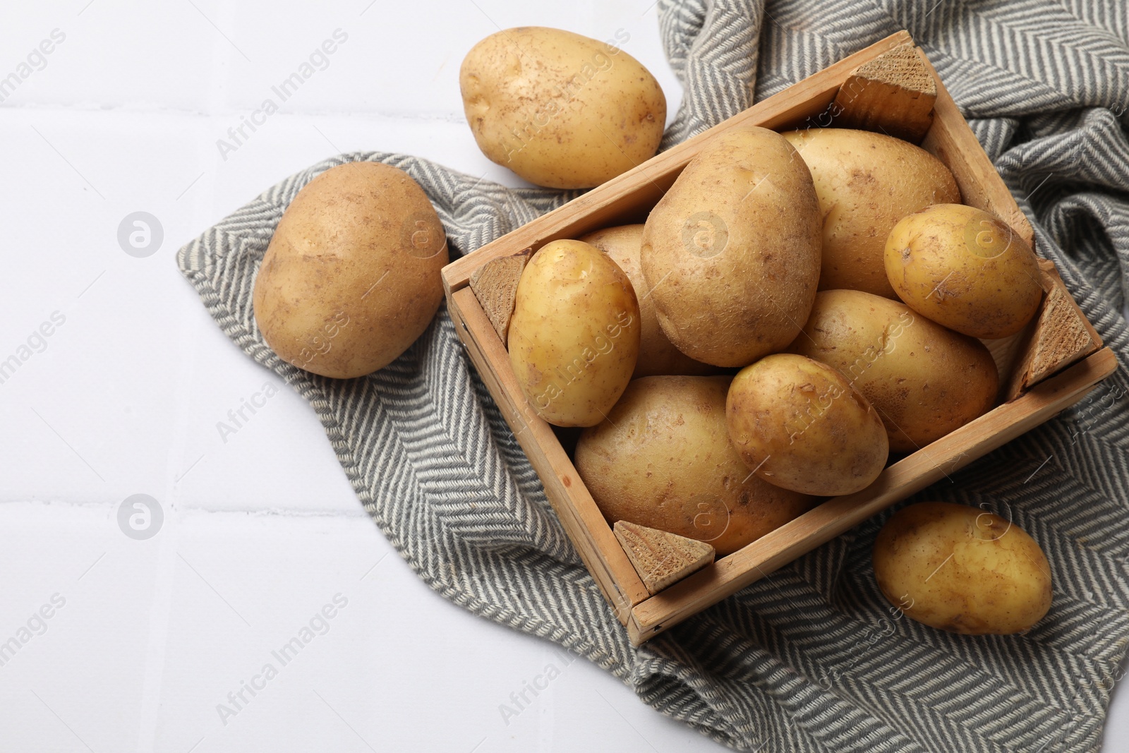 Photo of Raw fresh potatoes and wooden crate on white tiled table, top view