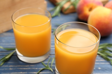 Photo of Glasses of natural peach juice on blue wooden table, closeup