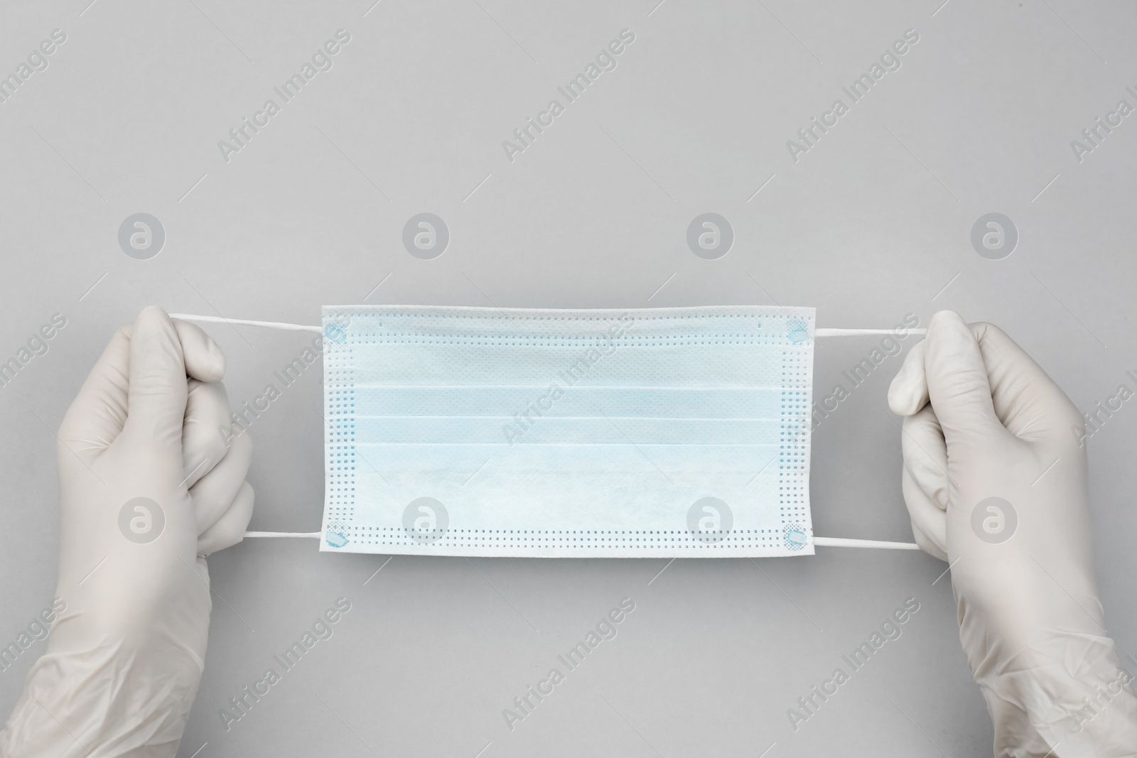 Photo of Doctor in medical gloves holding protective mask on light grey background, closeup. Space for text