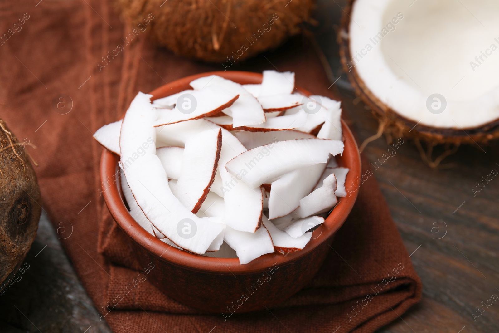 Photo of Coconut pieces in bowl and nut on wooden table, closeup