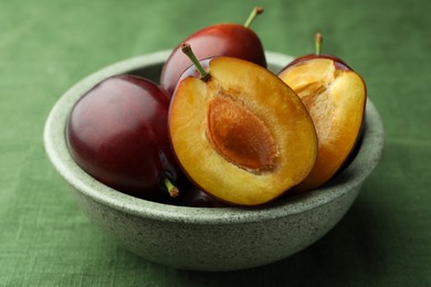 Photo of Many tasty ripe plums in bowl on green fabric, closeup