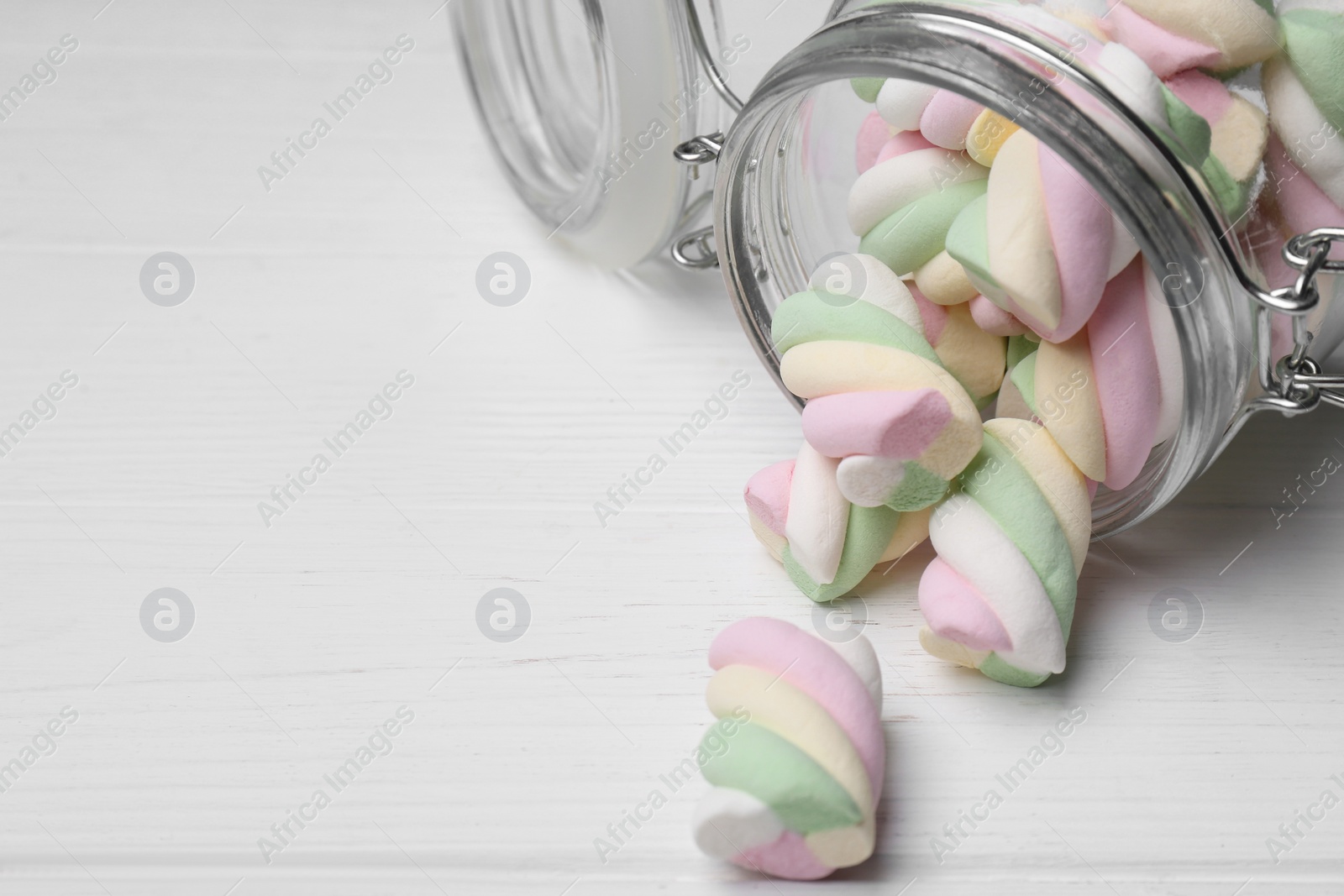 Photo of Glass jar with colorful marshmallows on white wooden table, closeup. Space for text