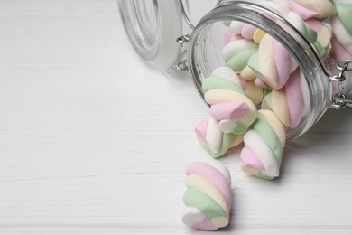 Photo of Glass jar with colorful marshmallows on white wooden table, closeup. Space for text