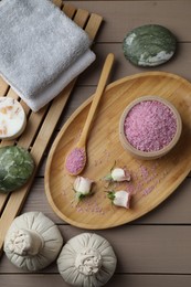 Bowl of pink sea salt, roses, spa stones, herbal massage bags and towels on wooden table, flat lay