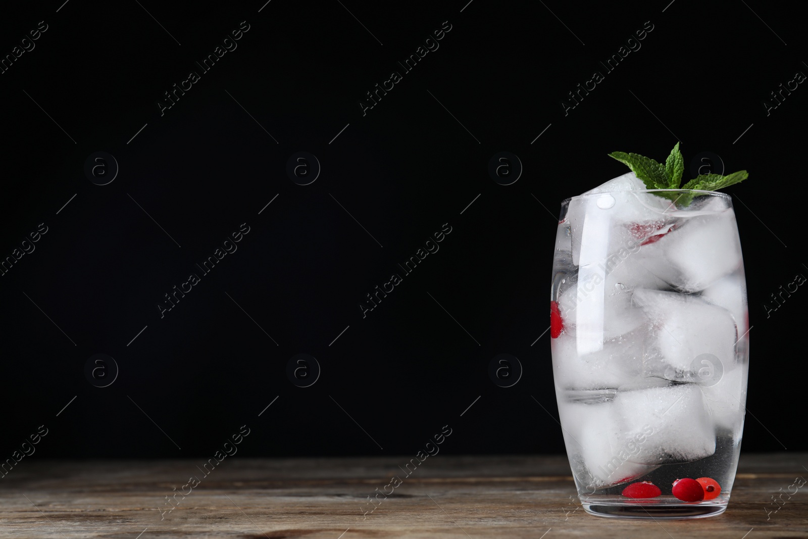 Photo of Vodka cocktail with cranberries and ice on wooden table against black background. Space for text