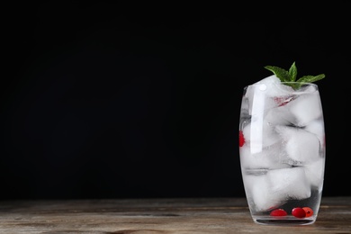 Photo of Vodka cocktail with cranberries and ice on wooden table against black background. Space for text