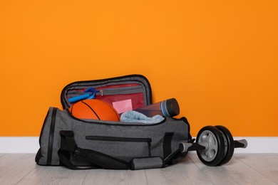 Photo of Gym bag and sports equipment on floor near orange wall