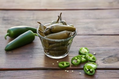 Photo of Fresh and pickled green jalapeno peppers on wooden table