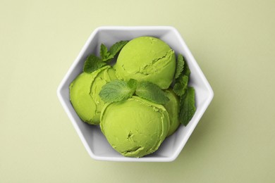 Photo of Tasty matcha ice cream with mint in bowl on pale green background, top view