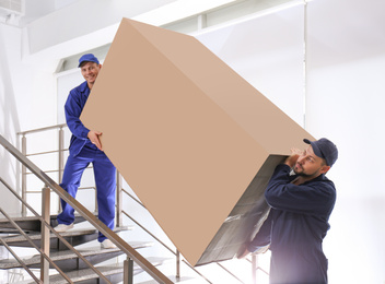 Professional workers carrying refrigerator on stairs indoors