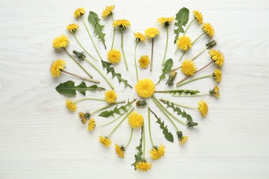 Photo of Heart made of beautiful yellow dandelions on white wooden table, flat lay