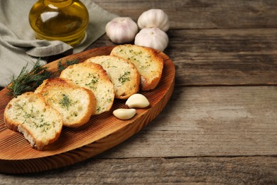 Photo of Tasty baguette with garlic, dill and oil on wooden table, space for text