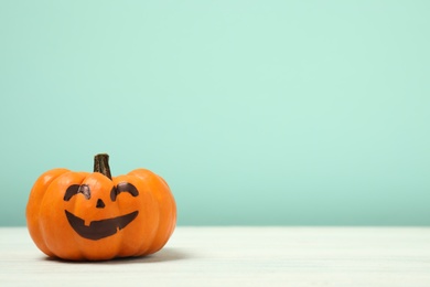 Photo of Pumpkin with scary face on light turquoise background, space for text. Halloween decor