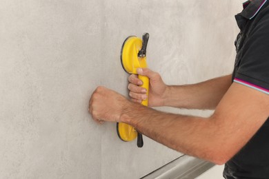 Photo of Worker installing wall tiles with vacuum holder indoors, closeup