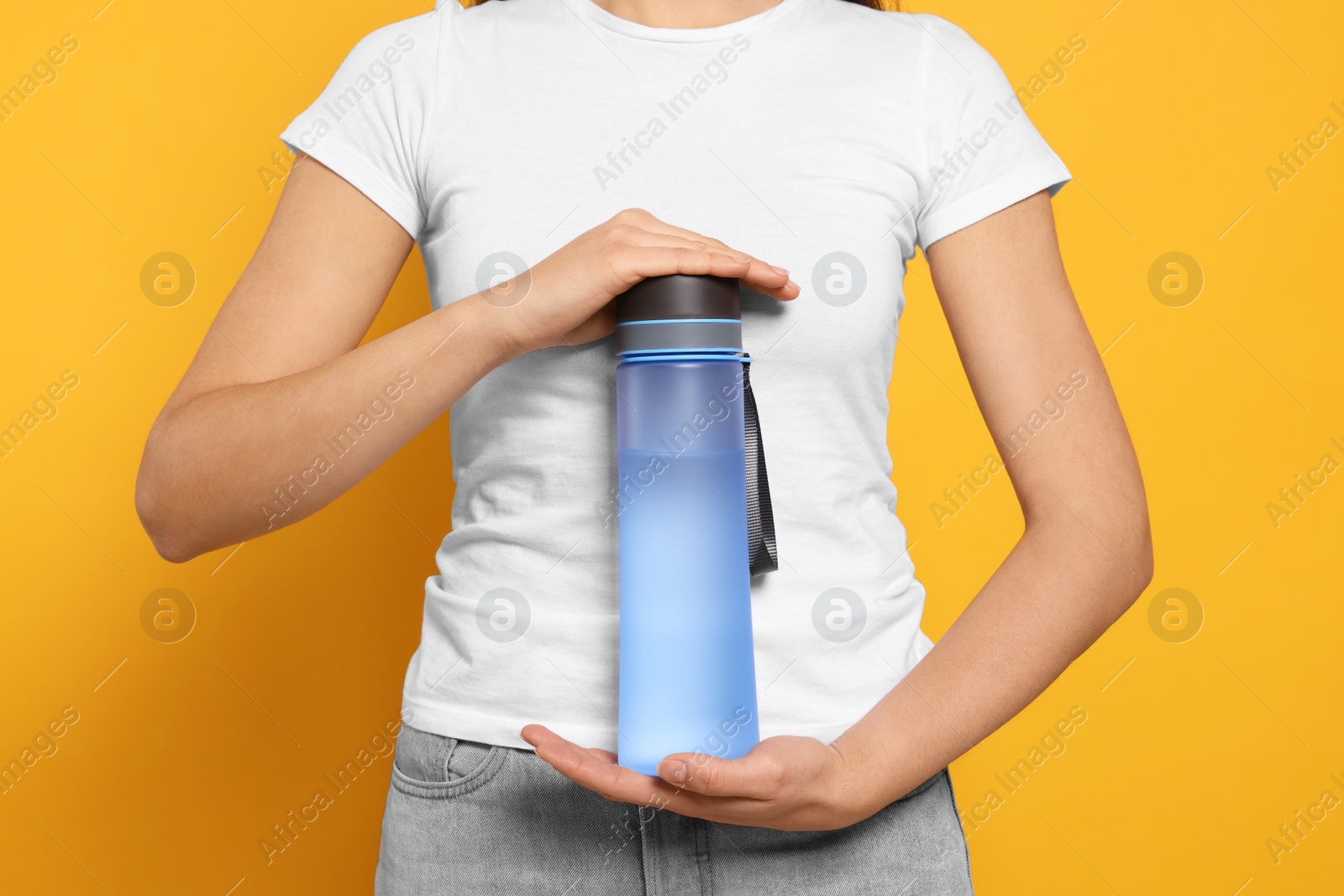 Photo of Woman holding bottle of water on orange background, closeup
