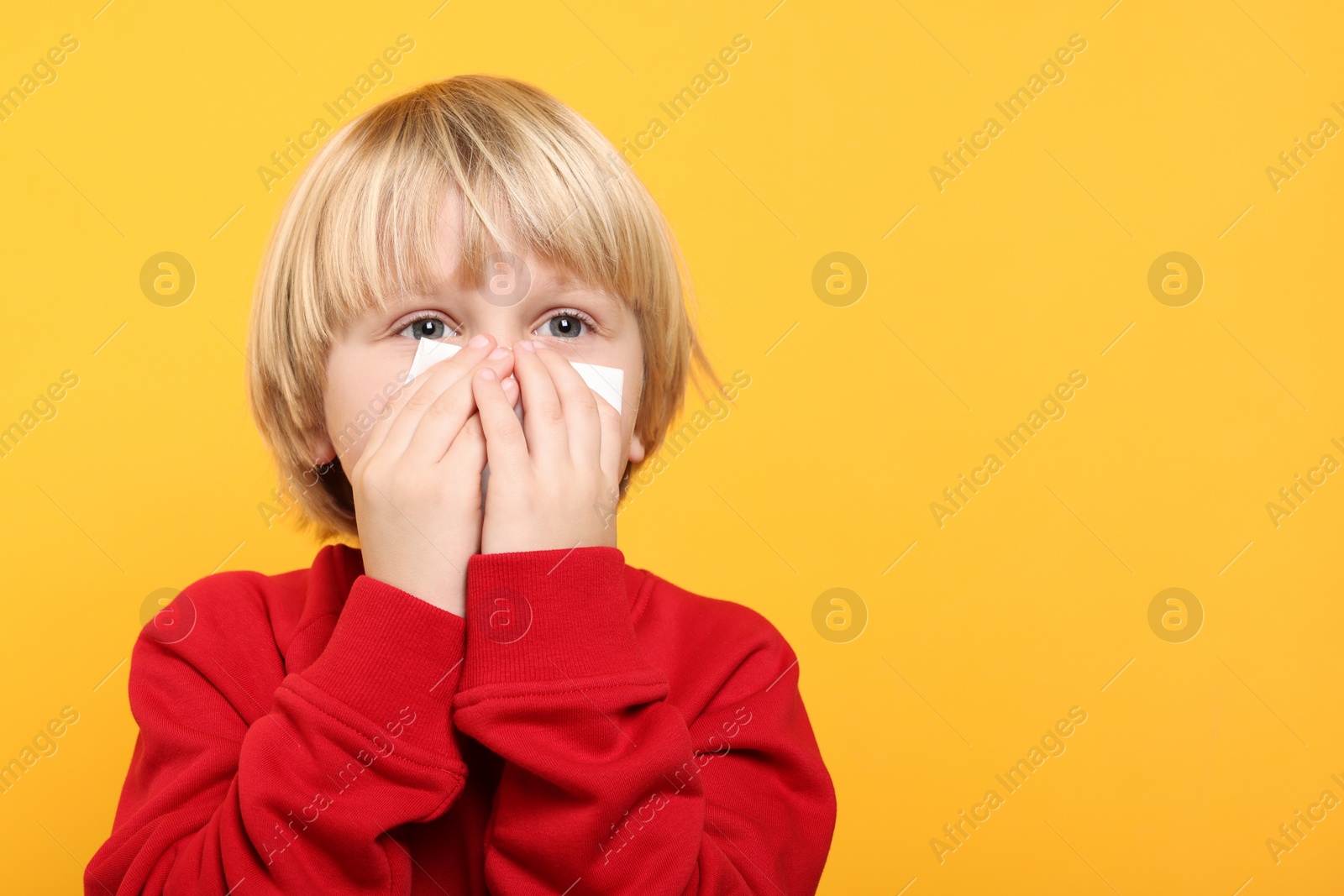 Photo of Boy blowing nose in tissue on orange background, space for text. Cold symptoms