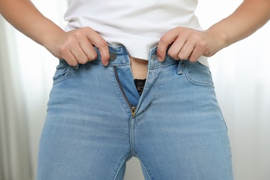 Photo of Woman trying to put on tight jeans indoors, closeup