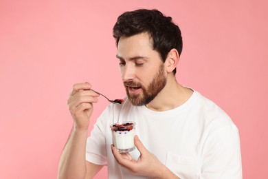 Handsome man eating delicious yogurt on pink background