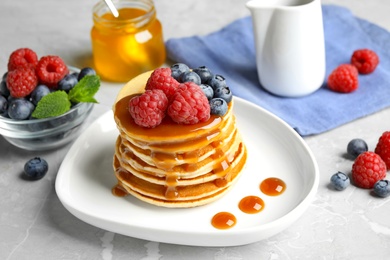 Photo of Delicious pancakes with fresh berries and syrup on grey table