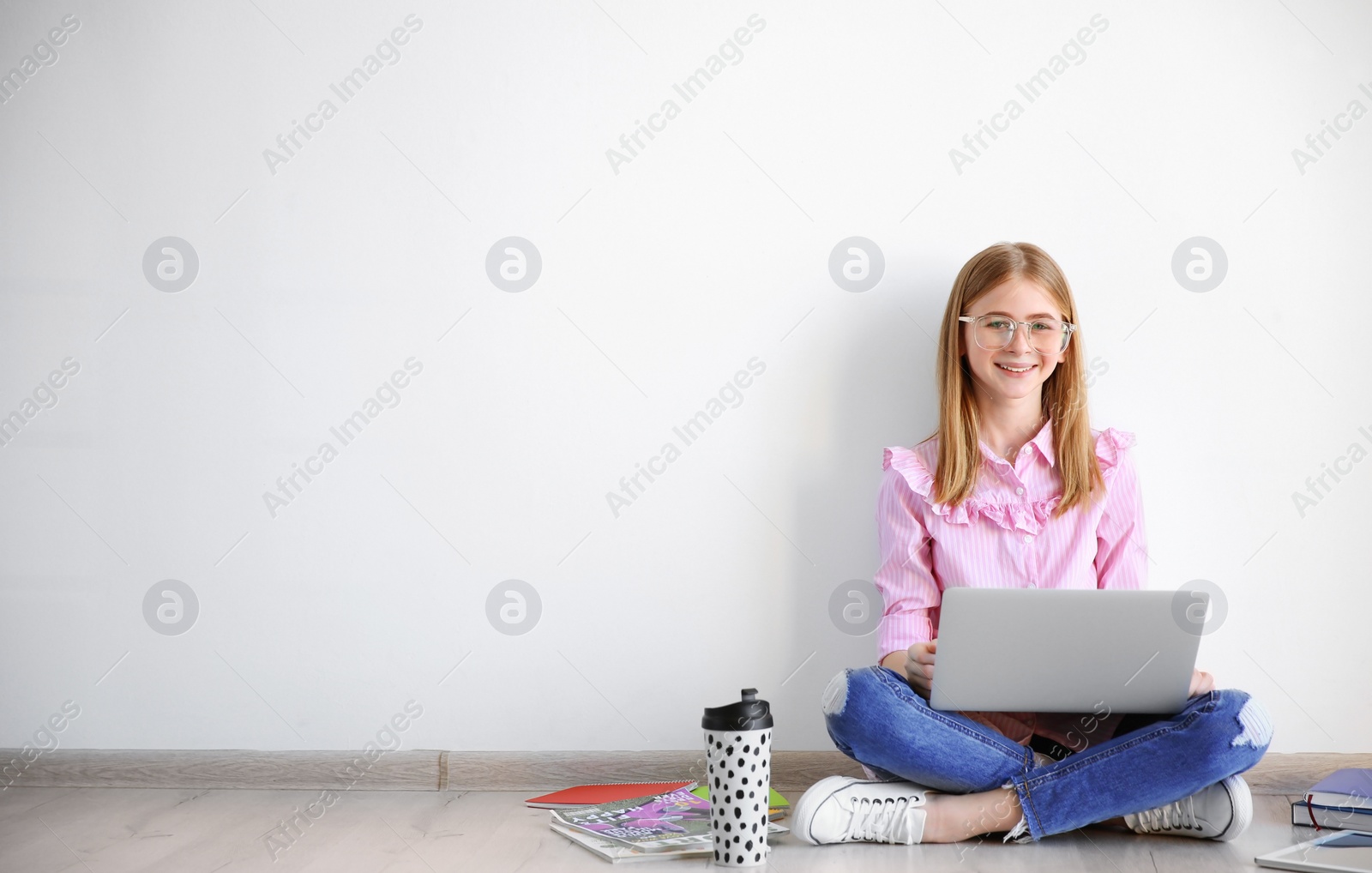 Photo of Cute teenage blogger with laptop sitting on floor against light wall