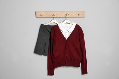 Photo of Shirt, jumper and skirt hanging on light wall. School uniform