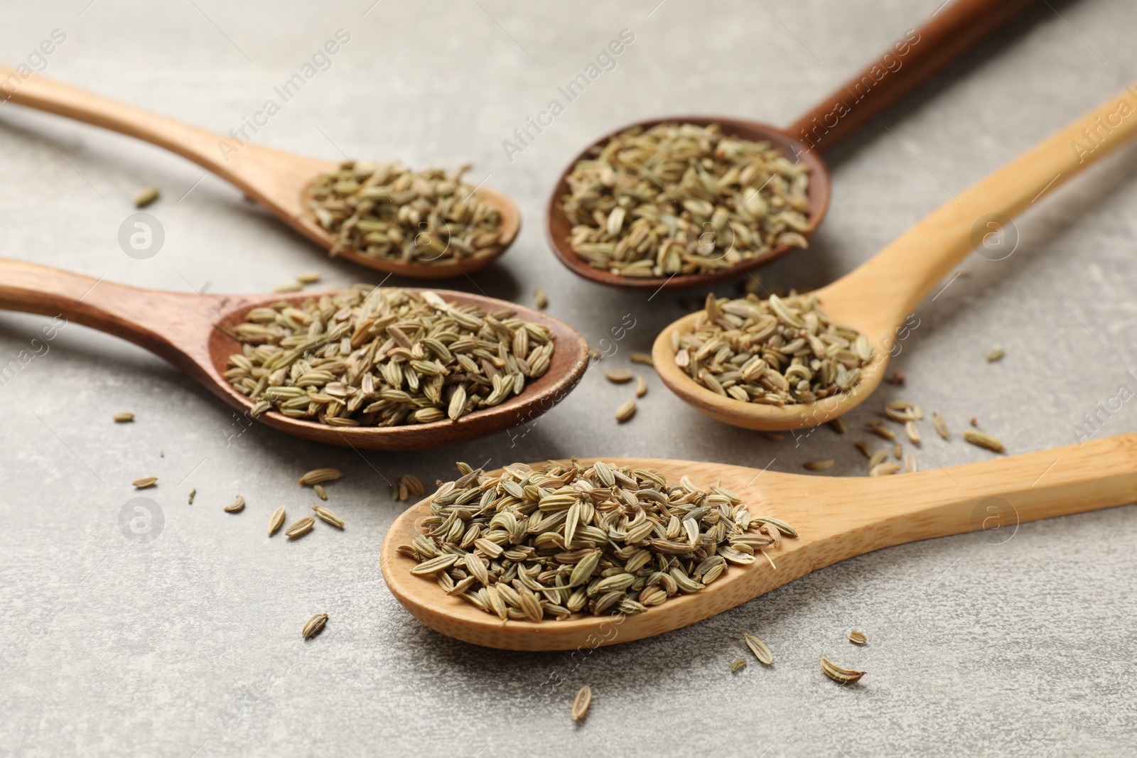 Photo of Wooden spoons with fennel seeds on grey table, closeup